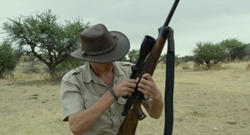 Movie still from “Safari” (2016), directed by Ulrich Seidl – A man holding a rifle in his hands; Medium shot, Low angle
