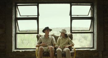 Movie still from “Safari” (2016), directed by Ulrich Seidl – A man and a woman sitting on a chair in front of a window; Wide shot, Over the shoulder angle