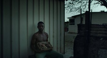 Movie still from “Safari” (2016), directed by Ulrich Seidl – A man sitting on a bench holding a box; Medium shot, Low angle