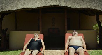 Movie still from “Safari” (2016), directed by Ulrich Seidl – A couple of people that are laying down on some chairs; Wide shot, Low angle