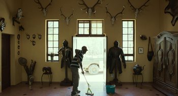 Movie still from “Safari” (2016), directed by Ulrich Seidl – A man mopping the floor in a room with statues; Wide shot, Low angle