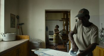 Movie still from “Safari” (2016), directed by Ulrich Seidl – A man and a woman in a kitchen with a ironing board; Medium shot, Over the shoulder angle