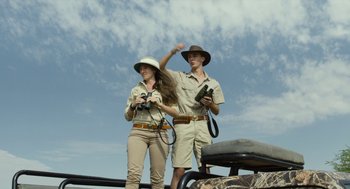 Movie still from “Safari” (2016), directed by Ulrich Seidl – A man and a woman standing next to each other holding binoculars; Medium shot, Low angle