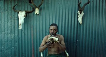 Movie still from “Safari” (2016), directed by Ulrich Seidl – A shirtless man eating a piece of food; Medium shot, Low angle