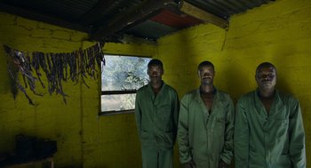 Movie still from “Safari” (2016), directed by Ulrich Seidl – A couple of men standing next to each other in a room; Medium shot, Low angle