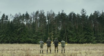Movie still from “Safari” (2016), directed by Ulrich Seidl – A group of men standing in a field with trees in the background; Extreme Wide shot, Low angle