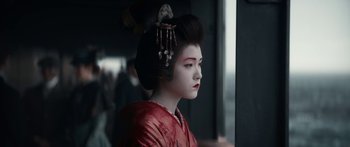 A geisha in a red dress is looking out a window