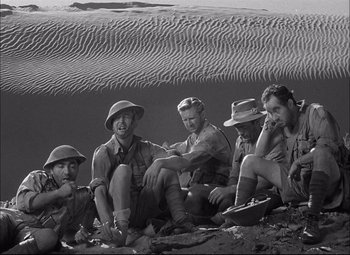 Movie still from “Sahara” (1943), directed by Zoltan Korda – A black and white photo of a group of men sitting on the ground; Wide shot, High angle