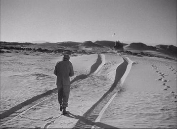 Movie still from “Sahara” (1943), directed by Zoltan Korda – A man is walking through the snow on a road; Wide shot, High angle