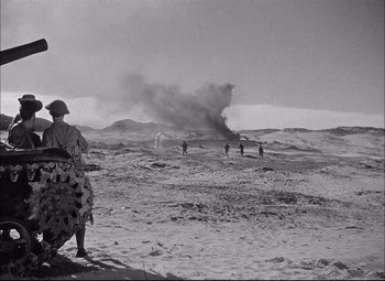 Movie still from “Sahara” (1943), directed by Zoltan Korda – A group of men standing on top of a sandy beach; Extreme Wide shot, Over the shoulder angle