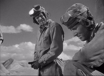 Movie still from “Sahara” (1943), directed by Zoltan Korda – A man wearing a helmet and goggles while standing next to another man; Medium shot, Low angle
