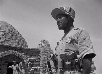 Movie still from “Sahara” (1943), directed by Zoltan Korda – An old black and white photo of a man standing in front of a brick building; Close Up shot, Low angle