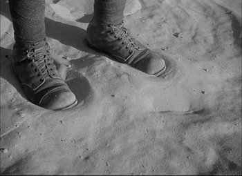 Movie still from “Sahara” (1943), directed by Zoltan Korda – A pair of feet in boots standing in the sand on the beach; Wide shot, High angle