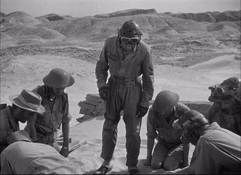 Movie still from “Sahara” (1943), directed by Zoltan Korda – A group of people in a field with a man in a gas mask; Wide shot, High angle