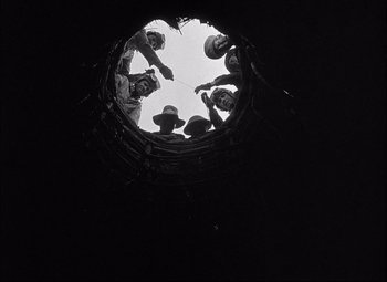 Movie still from “Sahara” (1943), directed by Zoltan Korda – A group of people standing in a circle in the middle of a tunnel; Wide shot, Overhead angle