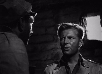 Movie still from “Sahara” (1943), directed by Zoltan Korda – A man and a man standing next to each other in front of a brick wall; Close Up shot, Over the shoulder angle