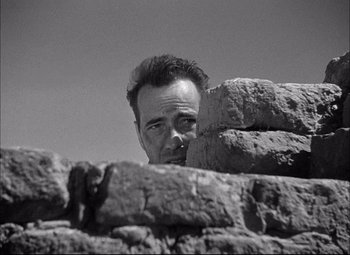 Movie still from “Sahara” (1943), directed by Zoltan Korda – A black - and - white photo of a man looking over a rock wall; Close Up shot, Low angle