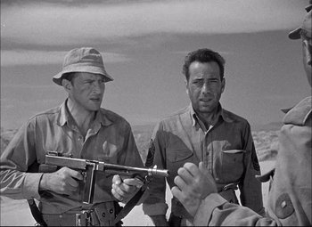 Movie still from “Sahara” (1943), directed by Zoltan Korda – A group of men standing next to each other holding guns; Medium shot, Over the shoulder angle