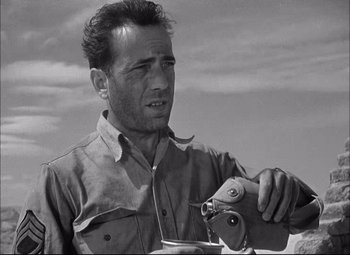 Movie still from “Sahara” (1943), directed by Zoltan Korda – A black and white photo of a man holding a camera; Close Up shot, Low angle