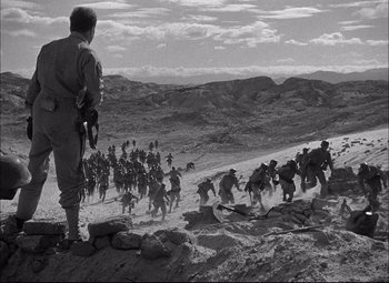 Movie still from “Sahara” (1943), directed by Zoltan Korda – A black - and - white photo of a group of men running across a field; Extreme Wide shot, Over the shoulder angle