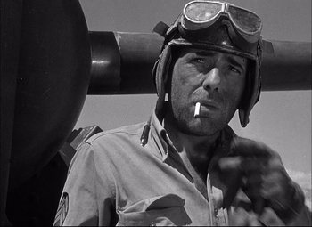 Movie still from “Sahara” (1943), directed by Zoltan Korda – A man wearing a helmet smoking a cigarette in front of an airplane; Close Up shot, Low angle