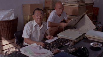 Movie still from “Saint Jack” (1979), directed by Peter Bogdanovich – Two men sitting in front of a computer keyboard; Medium shot, High angle