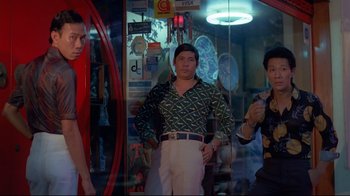 Movie still from “Saint Jack” (1979), directed by Peter Bogdanovich – A group of men standing next to each other in a room; Medium shot, Low angle