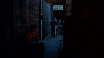 Movie still from “Saint Jack” (1979), directed by Peter Bogdanovich – A person walking down a street at night; Wide shot, High angle