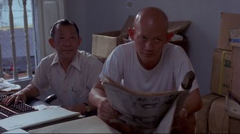Movie still from “Saint Jack” (1979), directed by Peter Bogdanovich – Two men are sitting at a table and one is reading a newspaper; Close Up shot, High angle