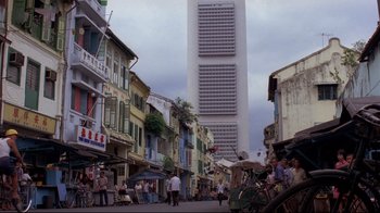 Movie still from “Saint Jack” (1979), directed by Peter Bogdanovich – People walking down a street in front of a tall building; Extreme Wide shot, Low angle