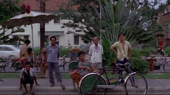 Movie still from “Saint Jack” (1979), directed by Peter Bogdanovich – A group of men standing next to a bicycle; Wide shot, High angle