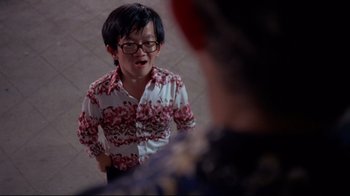 Movie still from “Saint Jack” (1979), directed by Peter Bogdanovich – A young man wearing glasses talking to a woman; Medium shot, Over the shoulder angle