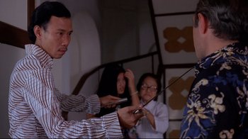 Movie still from “Saint Jack” (1979), directed by Peter Bogdanovich – A group of people standing around each other holding cell phones; Medium shot, Over the shoulder angle