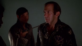 Movie still from “Saint Jack” (1979), directed by Peter Bogdanovich – A man in a hawaiian shirt is smoking a pipe; Close Up shot, Over the shoulder angle