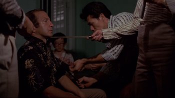 Movie still from “Saint Jack” (1979), directed by Peter Bogdanovich – A man cutting another man's hair with a pair of shears; Medium shot, Over the shoulder angle