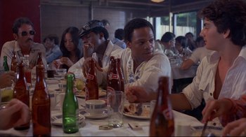 Movie still from “Saint Jack” (1979), directed by Peter Bogdanovich – A group of people sitting at a table eating food; Medium shot, Over the shoulder angle