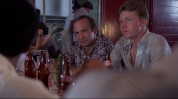 Movie still from “Saint Jack” (1979), directed by Peter Bogdanovich – A group of men sitting at a table with beer; Medium shot, Over the shoulder angle