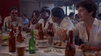 Movie still from “Saint Jack” (1979), directed by Peter Bogdanovich – A group of people sitting at a table eating food; Medium shot, Over the shoulder angle