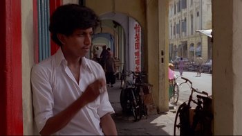 Movie still from “Saint Jack” (1979), directed by Peter Bogdanovich – A man in a white shirt is walking down the street; Medium shot, Low angle