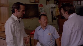 Movie still from “Saint Jack” (1979), directed by Peter Bogdanovich – A group of people standing around in a room together; Medium shot, Low angle