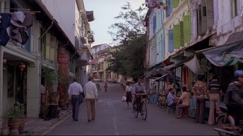 Movie still from “Saint Jack” (1979), directed by Peter Bogdanovich – A group of people walking down a street near buildings; Extreme Wide shot, High angle