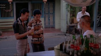 Movie still from “Saint Jack” (1979), directed by Peter Bogdanovich – Two men standing next to each other in front of a table; Medium shot, Over the shoulder angle