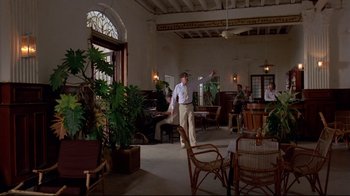 Movie still from “Saint Jack” (1979), directed by Peter Bogdanovich – A group of people sitting in a room with potted plants; Wide shot, Low angle