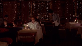 Movie still from “Saint Jack” (1979), directed by Peter Bogdanovich – A man sitting at a table with a lit candle in front of him; Wide shot, High angle