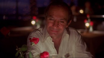 Movie still from “Saint Jack” (1979), directed by Peter Bogdanovich – A person sitting at a table with a rose; Close Up shot, Low angle