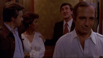 Movie still from “Saint Jack” (1979), directed by Peter Bogdanovich – A man and a woman are standing next to each other in front of other men; Medium shot, Over the shoulder angle