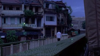 Movie still from “Saint Jack” (1979), directed by Peter Bogdanovich – A man walking on a bridge near some buildings; Extreme Wide shot, Low angle