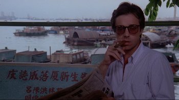 Movie still from “Saint Jack” (1979), directed by Peter Bogdanovich – A man sitting in front of a window holding a cigarette; Close Up shot, Low angle