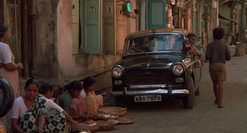 Movie still from “Salaam Bombay!” (1988), directed by Mira Nair – A black car parked on the side of the street; Wide shot, High angle