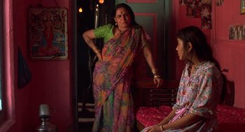 Movie still from “Salaam Bombay!” (1988), directed by Mira Nair – A woman in a colorful sari standing next to another woman; Medium shot, Over the shoulder angle